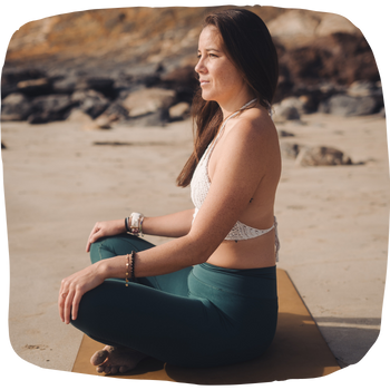 Vannaly assise en tailleur face à la mer lors d'un cours de yoga en plein air